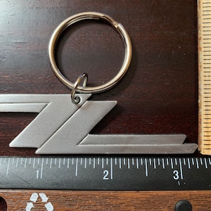 May include: A silver metal keychain with a stylized 'Z' design. The keychain is attached to a silver metal ring.
