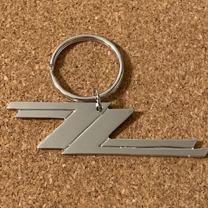 May include: A silver metal keychain with a stylized lightning bolt design. The keychain has a silver metal ring.