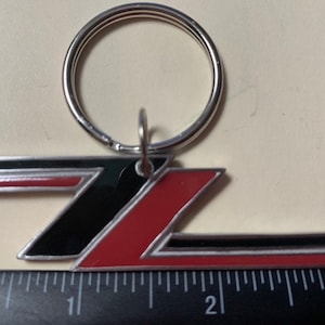 May include: A silver key chain with a red and black metal logo of the letter "Z" with a silver ring.
