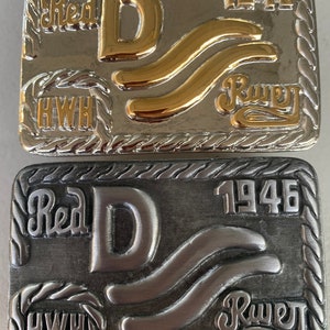 May include: A silver belt buckle with a gold-colored 'D' and 'R' in the center. The buckle also has the text 'Red D 1946' and 'HWH' on it.