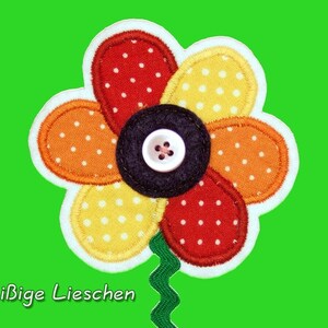 Puede incluir: Una flor de fieltro colorida con un botón negro en el centro. La flor tiene cinco pétalos en tonos de rojo, naranja y amarillo con lunares blancos. La flor está unida a un tallo verde.