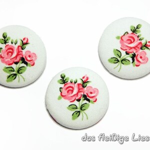 May include: Three white fabric-covered buttons with a floral design. Each button features a cluster of pink roses with green leaves. The buttons are round and have a vintage, handmade aesthetic. The text "das fleißige Lieschen" is visible.