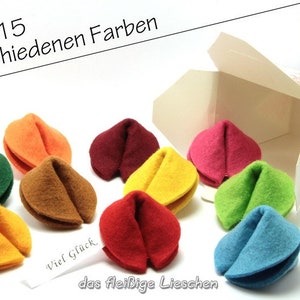Pode incluir: Um conjunto de 9 biscoitos da sorte de feltro em várias cores, incluindo vermelho, verde, amarelo, azul, marrom e laranja, em um recipiente de comida para viagem branco. O texto "in 15 verschiedenen Farben" é visível na imagem.