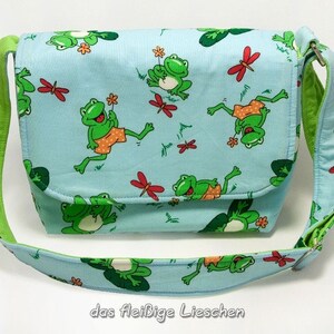 Può includere: Una borsa a tracolla blu chiaro con una tracolla verde e una stampa di rane. La borsa ha il testo "das fleißige Lieschen" stampato sul fondo.