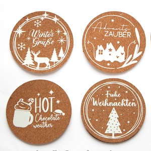 May include: Four round cork coasters with white designs. The coasters feature winter-themed illustrations and text, including "Winter Grüße", "Adventzauber", "Hot Chocolate Weather", and "Frohe Weihnachten".