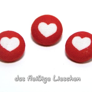 Könnte beinhalten: Drei rote Stoffknöpfe mit weißen Herzmotiven.