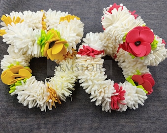 May include: Circular floral garlands with white, yellow, red, and green accents. The garlands are made of soft, textured material, with a ring shape. The background is a solid gray color. The garlands are likely used for decoration or as accessories.