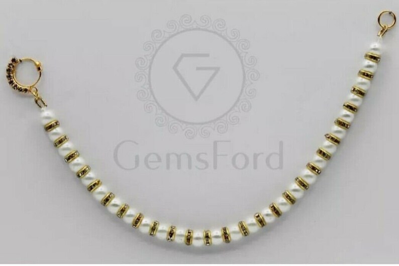 May include: A white and gold nose ring with a pearl and rhinestone design. The nose ring is attached to a chain with white pearls and gold accents.