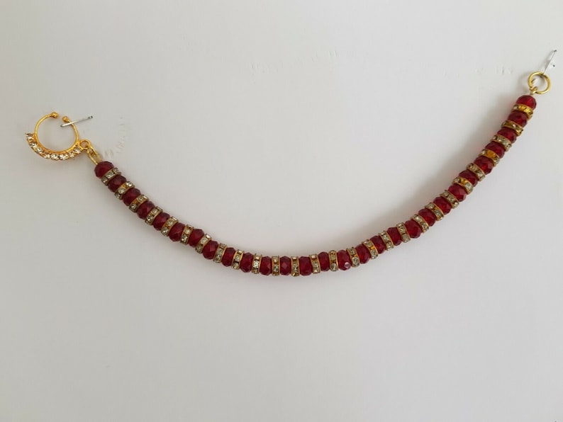 May include: A gold nose ring with a red and clear beaded chain.