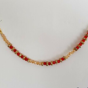 May include: A gold nose ring with a chain of red and beige beads. The chain is attached to a small hoop.