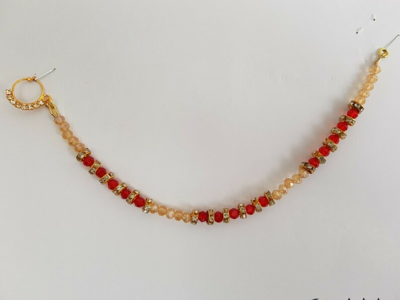 May include: A gold nose ring with a chain of red and beige beads. The chain is attached to a small hoop.