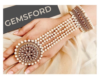 May include: A gold and white ring with a large, round, jeweled centre piece. The ring is attached to a long, white pearl bracelet.