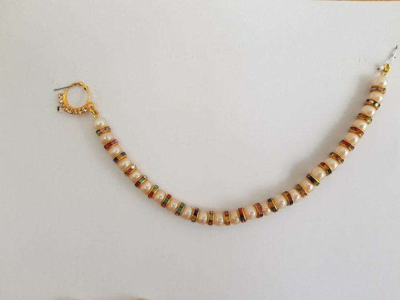 May include: A gold nose ring with a chain of white pearls and colourful rhinestones.