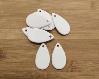 May include: A set of seven white ceramic teardrop-shaped pendants with a hole at the top. The pendants are arranged in a pile on a wooden surface.