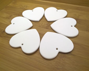 May include: Six white ceramic heart-shaped ornaments with a hole at the top for hanging.