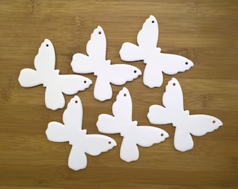 May include: Six white ceramic butterfly ornaments with a simple design. The butterflies are all the same size and shape, and they have a hole at the top for hanging.