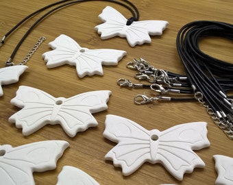 May include: A collection of white ceramic butterfly charms with black cords and silver clasps. The charms are arranged on a wooden surface.