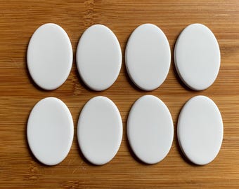 May include: Eight white oval ceramic tiles arranged in two rows of four on a wooden surface.