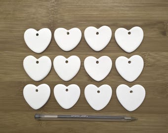 May include: Twelve white ceramic heart-shaped ornaments with a hole at the top for hanging.