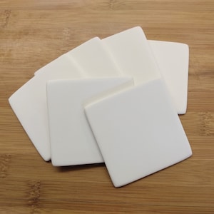 May include: Set of six white ceramic coasters. The coasters are square shaped and have a smooth, matte finish.
