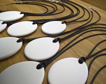 May include: Several white oval pendants on black cords with silver clasps. The pendants are arranged on a wooden surface. The cords are knotted at the top of each pendant.