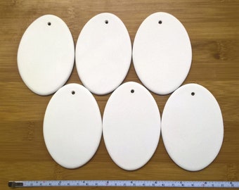 May include: Six white ceramic oval ornaments with a hole for hanging. The ornaments are blank and ready to be painted or decorated.
