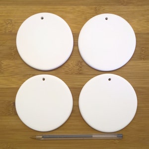 May include: Four white ceramic round baubles with a hole for hanging. The baubles are on a wooden surface.