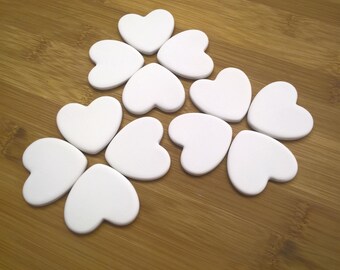 May include: A set of 10 white heart-shaped ceramic tiles arranged in a flower pattern on a wooden surface.