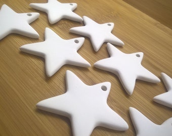 May include: A set of ten white ceramic star-shaped ornaments. The stars are all the same size and shape, and they have a hole at the top for hanging.