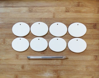 May include: Eight white ceramic round ornaments with a hole in the center, arranged in two rows of four on a wooden surface. A silver pen is lying below the ornaments.