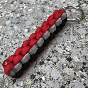 May include: A red, grey, and black paracord keychain with a silver key ring.