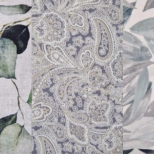Könnte beinhalten: Ein Stoffpaneel mit drei verschiedenen Mustern. Ein Abschnitt zeigt grüne Eukalyptusblätter, ein anderer ein Paisley-Design in Grau und Weiß, und der dritte graue und blaue Blätter auf weißem Hintergrund. Das Gesamtthema ist botanisch.