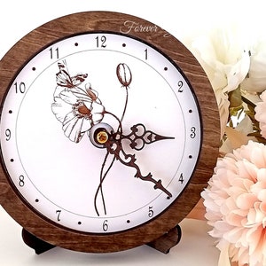 May include: A wooden clock with a white face and a floral design. The clock has Roman numeral hour markers and black hands. The clock is on a wooden stand.