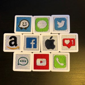 May include: Nine white square tiles with different coloured backgrounds and embroidered logos. The logos include: Amazon, Facebook, Apple, Instagram, Snapchat, Twitter, YouTube, WhatsApp, and a ghost.