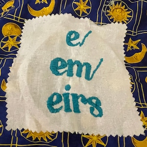 May include: A white, rectangular patch with teal embroidery spelling out the word "emers". The patch has a scalloped edge and is set against a blue fabric with gold celestial patterns including moons, stars, and suns.