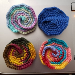 May include: Four crocheted flower embellishments in different color combinations. The flowers are made with a spiral pattern and have a three-dimensional appearance.