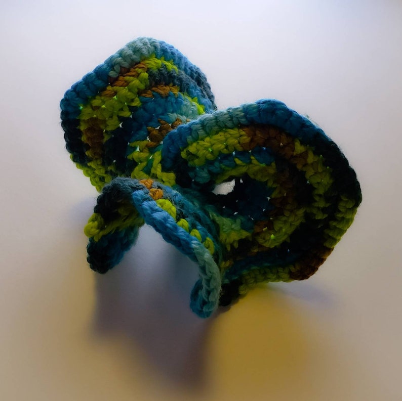 May include: A crocheted sculpture with a swirling, organic shape. It is made with blue, green, and brown yarn.