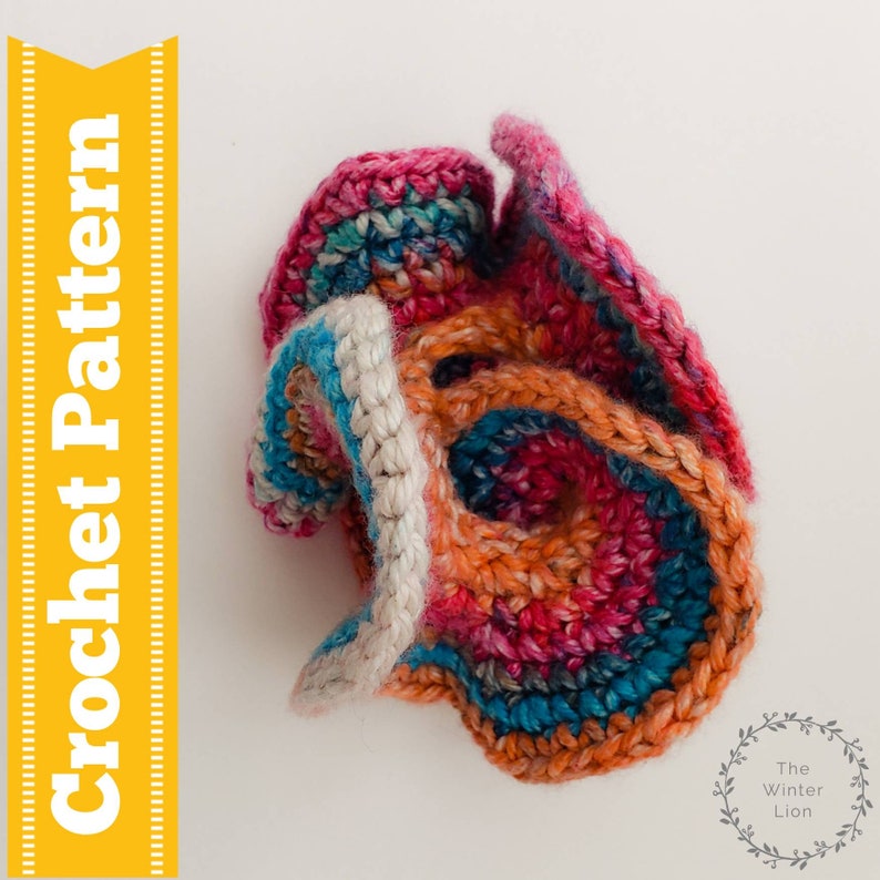 May include: A colorful crocheted flower with a white center. The flower is made with a variety of shades of pink, orange, blue, and teal yarn.