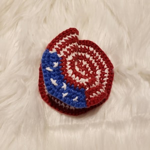 May include: A crocheted hat in the shape of a circle with red, white, and blue yarn. The hat is folded in half and the red and white yarn is on the outside.