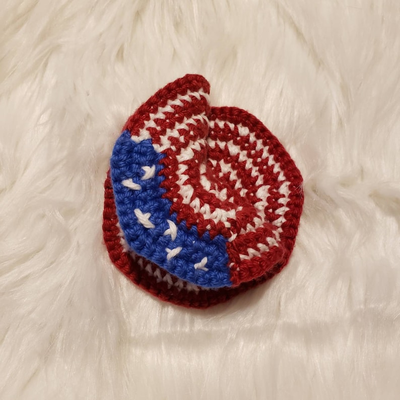 May include: A crocheted hat in the shape of a circle with red, white, and blue yarn. The hat is folded in half and the red and white yarn is on the outside.