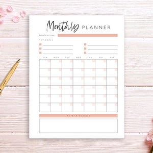 May include: A printable monthly planner with a pink and white color scheme. The planner includes sections for month and year, top goals, notes and doodles, and a calendar grid with days of the week labeled.