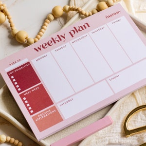 Könnte beinhalten: Ein rosa Wochenplaner mit einem roten Farbverlauf auf der linken Seite. Der Planer hat Abschnitte für jeden Tag der Woche mit Platz für "Top Priorities", "Next Week" und "Positive Affirmations". Der Planer enthält auch den Text "Print Pantry" in der oberen rechten Ecke.