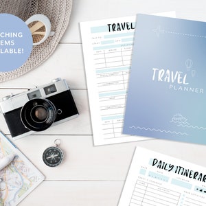 May include: A blue and white travel planner with a cover that says "TRAVEL PLANNER" and has illustrations of a plane, hot air balloon, and a boat. The planner includes sections for daily itinerary, travel details, and packing lists.