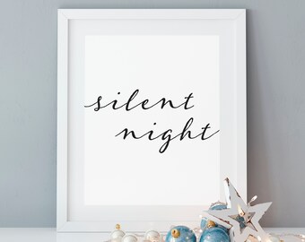 May include: A white framed print with the text "silent night" in black cursive script. The print is sitting on a white surface with blue and white Christmas ornaments and a white star.