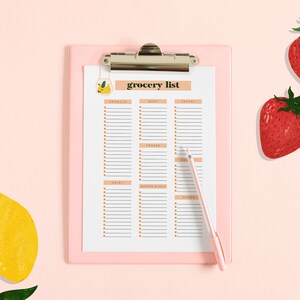 May include: A pink clipboard with a white grocery list on it. The list is divided into categories: produce, meat, pantry, frozen, dairy, bakery & bread, and other. There is a pen next to the clipboard. There are two red strawberries and two yellow lemons on a pink background.