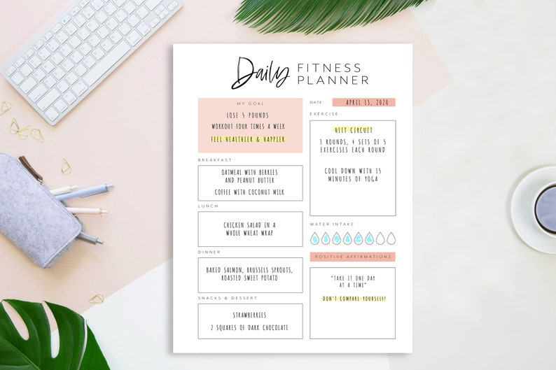 Op de afbeelding: Een printbare dagelijkse fitnessplanner met een roze en gele kleurschema. De planner bevat secties voor doelen, oefening, waterinname, positieve affirmaties en maaltijdplanning. De datum is 13 april 2020.