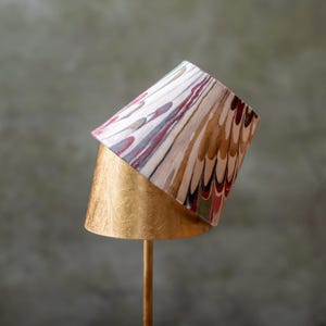 May include: A decorative lamp with a gold base and a patterned lampshade. The lampshade features a design with red, brown, and gold hues. The lamp is on a gold stand.
