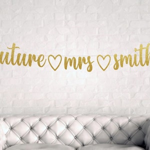 May include: Gold glitter banner with the text "future mrs smith" and hearts between the words.
