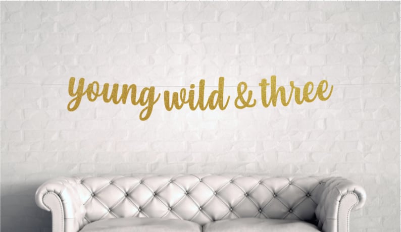 Puede incluir: Pancarta de purpurina dorada con el texto "young wild & three".