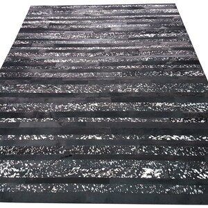 Puede incluir: Alfombra de piel de vaca rayada en blanco y negro con un aspecto desgastado. La alfombra está hecha de piel de vaca natural y tiene un estilo rústico único.
